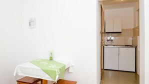 Et lille, rent rum med et bord og bænk, et tekøkken med hvide skabe og et flisegulv.