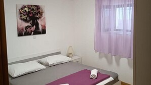 Een slaapkamer met een bed, nachtkastje, lamp, raam met paarse gordijnen en een schilderij aan de muur.