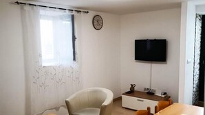 Een woonkamer met een bank, een houten salontafel, een eettafel met stoelen, een televisie aan de muur en een klok.