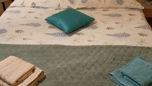 A neatly made bed with a floral bedspread, a teal pillow, and folded towels on the side. - Apartments Magda- Backside Studio Apartment (Cavtat)