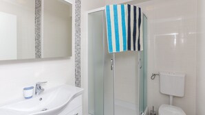 Un baño moderno con ducha de vidrio, lavamanos blanco y retrete.