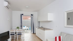 Un espacio habitable compacto con kitchenette, comedor y sofá con un cojín rojo y blanco.