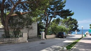 Rua com carro estacionado, árvores e um edifício com fachada de pedra.