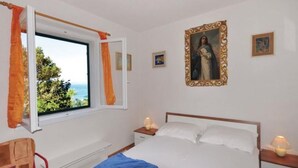 Quarto com cama, mesas de cabeceira, janela com cortinas, uma cadeira e um quadro na parede.