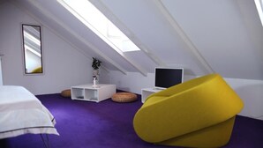 A modern, compact room with a sloped ceiling, a bed, a yellow bean bag, a small white table with a plant, and a flat-screen TV. - Apartments & Rooms Lejletul- Deluxe Studio Apartment (A2) (Dubrovnik)
