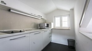 A compact kitchen with white cabinets, a microwave, and a window with blinds. - Apartments & Rooms Lejletul- Deluxe Studio Apartment (A2) (Dubrovnik)