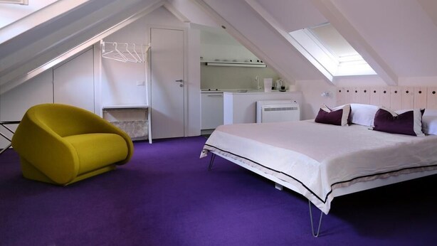 A bedroom with a bed, a yellow chair, a small kitchenette, and a skylight. - Apartments & Rooms Lejletul- Deluxe Studio Apartment (A2) (Dubrovnik)