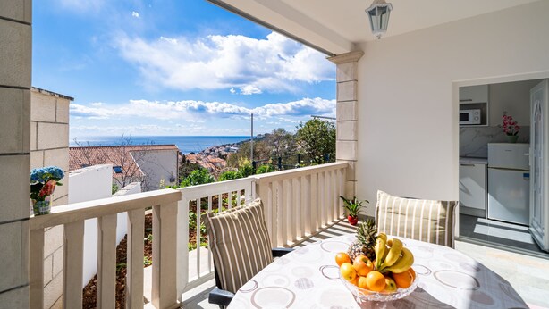 Ein Balkon mit Frühstückstisch, Blick auf das Meer und einer Küchenzeile.