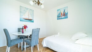 Ein Zimmer mit einem Bett, einem Esstisch mit Stühlen und zwei Bildern an den Wänden.