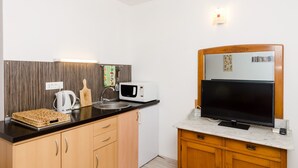 Una cocina compacta con microondas, hervidor y un televisor de pantalla plana sobre una encimera de mármol.