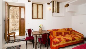Una habitación con pared de piedra, puerta de madera, una mesa redonda con sillas, un sofá y una alfombra pequeña.