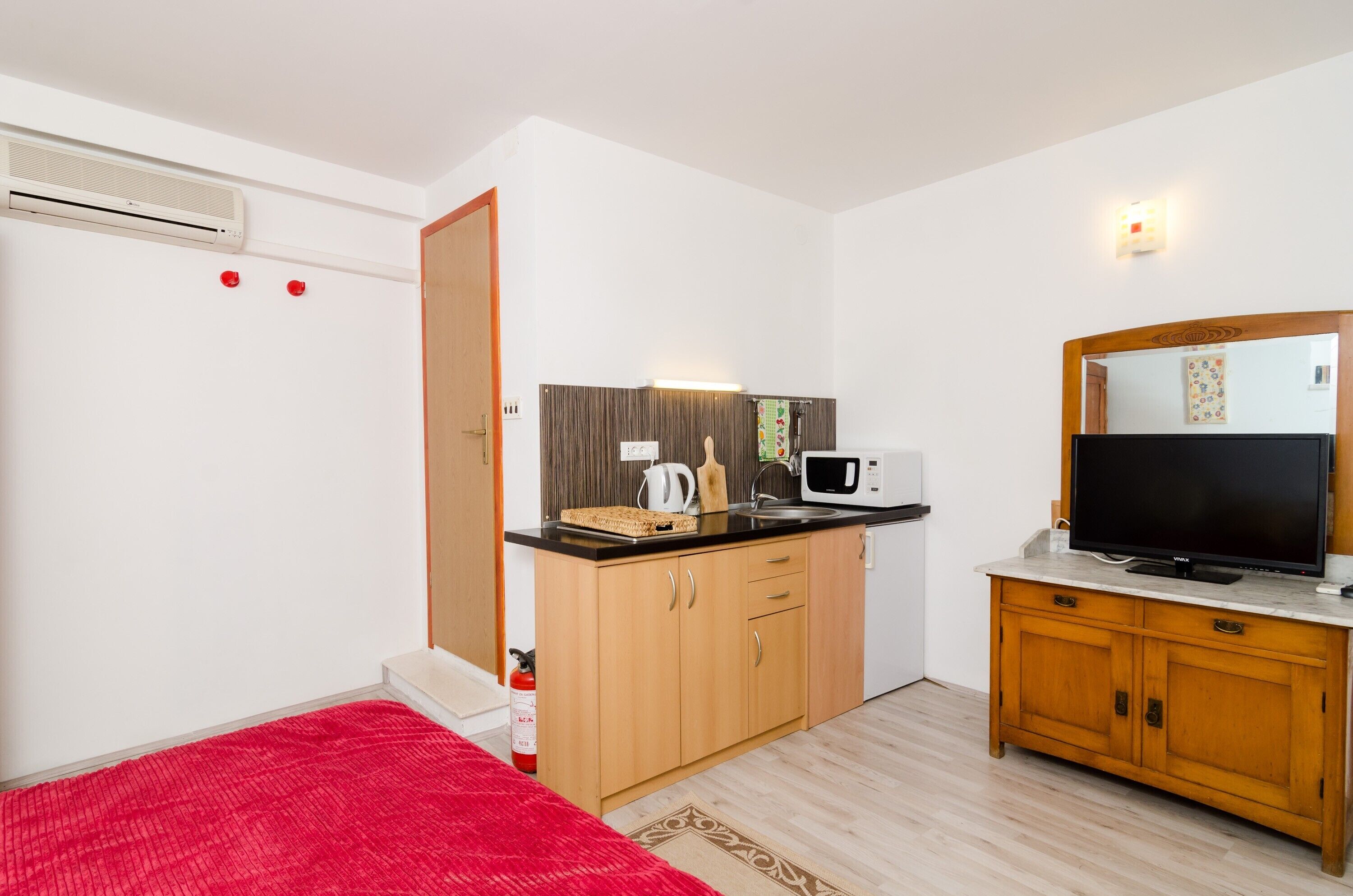 A compact kitchen with a microwave, kettle, and a flat-screen TV on a wooden cabinet.