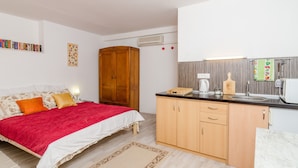 Un dormitorio con cama, mesita de noche, armario de madera y una zona de cocina con fregadero, estufa y microondas.