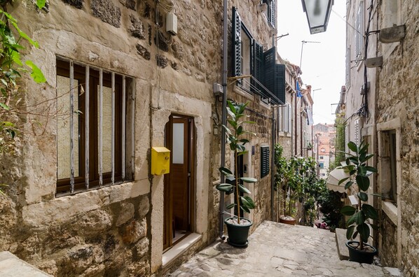 Une ruelle étroite pavée de pierres, bordée de bâtiments en pierre, avec une porte en bois et des plantes en pot.