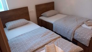 A room with two single beds, each with a wooden headboard, a bedside table, and a patterned bedspread.