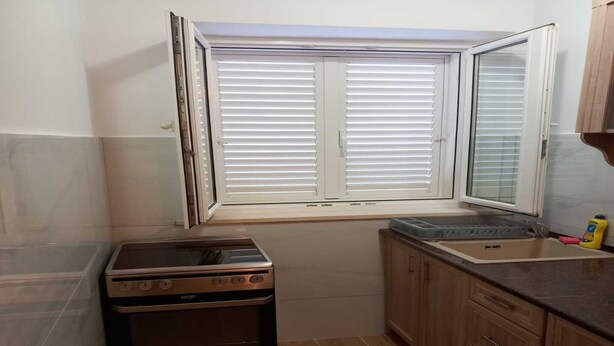A compact kitchen with a built-in oven, a window with blinds, and wooden cabinets.