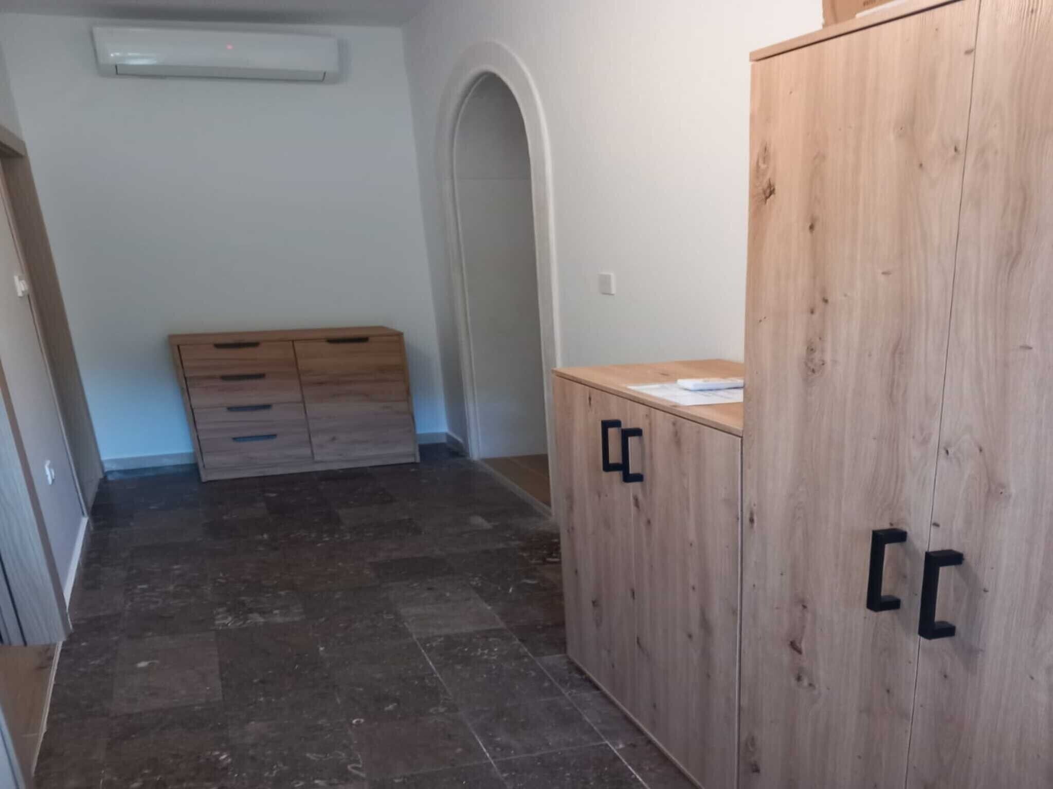Een kamer met een houten garderobe, een klein bureau met papieren en een betegelde vloer.