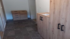 A room with a wooden wardrobe, a small desk with papers, and a tiled floor.