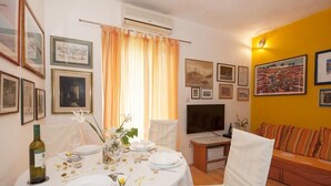 A dining area with a table set for four, a television, and a sofa in a room with yellow walls and framed pictures. - Apartments Kalajzic- One-Bedroom Apartment with Terrace (Pucisca)