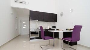 A modern kitchen with dark cabinets, a white countertop, and two purple chairs. - LUV Luxury Apartments - Studio Apartment with Balcony and Sea View (Dubrovnik)