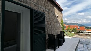 Een stenen gebouw met een garagepoort, een terras met stoelen en een uitzicht op de stad en de bergen op de achtergrond.