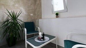 Een kleine kamer met een betegelde muur, een raam, een potplant, een stoel en een tafel met een dienblad.