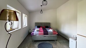 Een slaapkamer met een bed, een bureau, een lamp, een hanglamp, een raam en een koelkast.