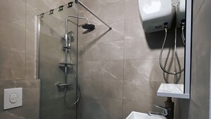 Een moderne badkamer met een douche met glazen wand, een witte wastafel en een spiegel erboven.