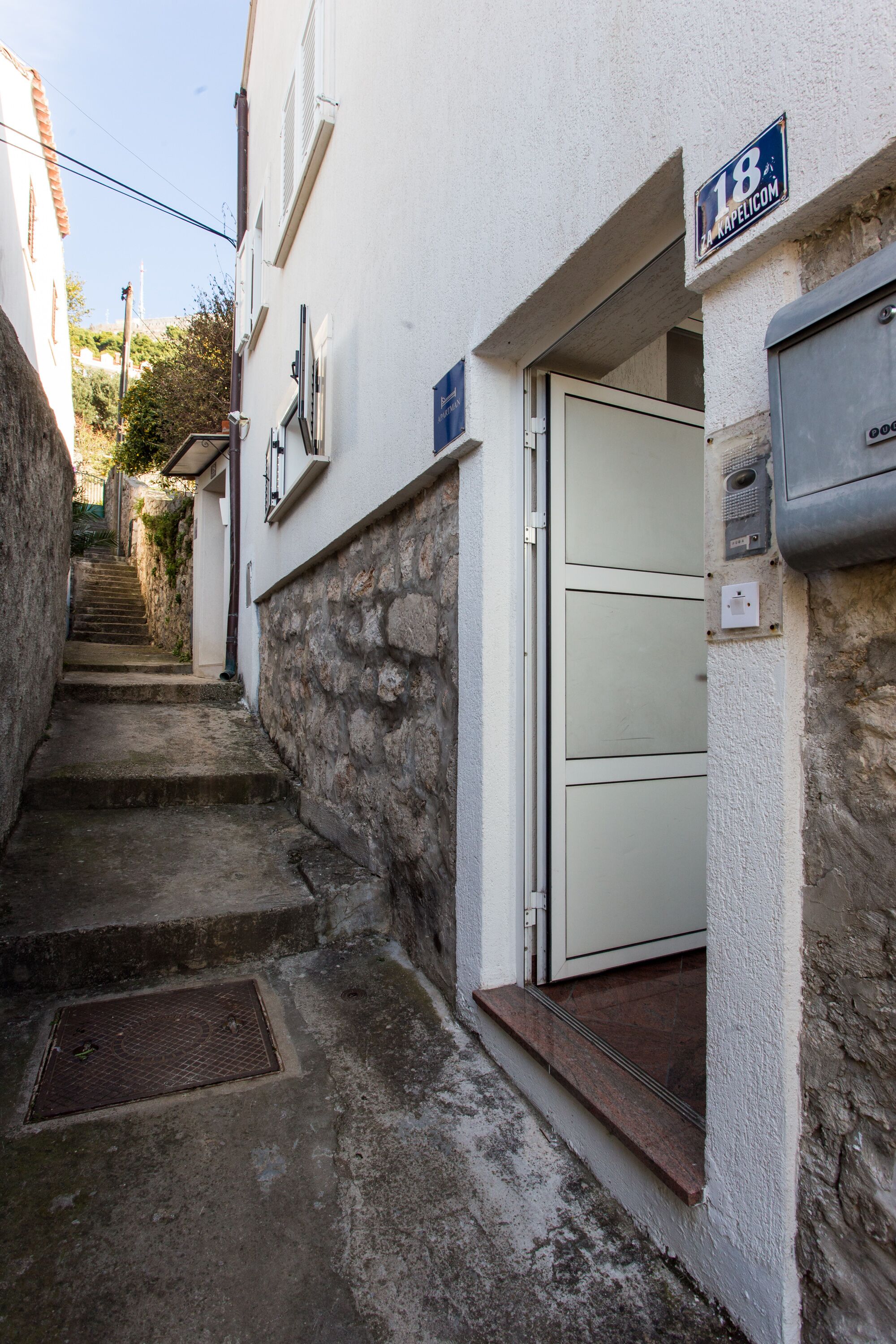 A narrow stone staircase leading to a white building with a metal door and a sign indicating the number 18.