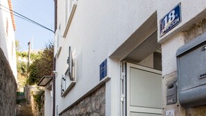 Eine schmale Steintreppe führt zu einem weißen Gebäude mit einer Metalttür und einem Schild mit der Nummer 18.