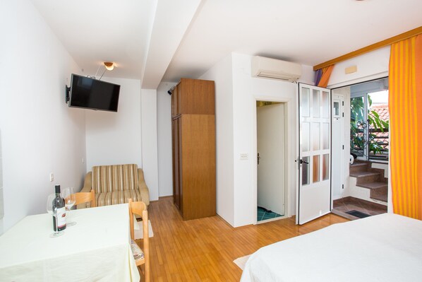 Une chambre d’hôtel comprenant un lit, un téléviseur fixé au mur, une table à manger avec des chaises et une porte en bois donnant sur un balcon.