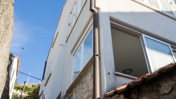 Ein zweistöckiges Gebäude mit einer Stein-Fassade und einem Metallgeländer im oberen Bereich, sowie einer sichtbaren Tür im Erdgeschoss.