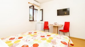 Une pièce avec un lit, deux chaises rouges, une petite table, un téléviseur et une fenêtre avec des rideaux.