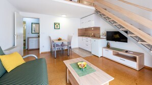 Un espacio habitable compacto con sofá, mesa de comedor, zona de cocina y una escalera.