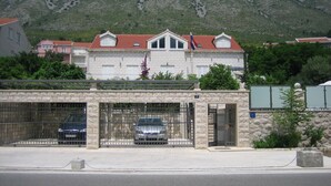 A two-story building with a red-tiled roof, a stone facade, and a gated entrance with two cars parked inside. - Villa Celenca - Two Bedroom Apartment with Terrace and Pool View (Mokosica)