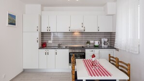 A modern kitchen with white cabinets, stainless steel appliances, and a dining area with a checkered tablecloth. - Villa Celenca - Two Bedroom Apartment with Terrace and Pool View (Mokosica)
