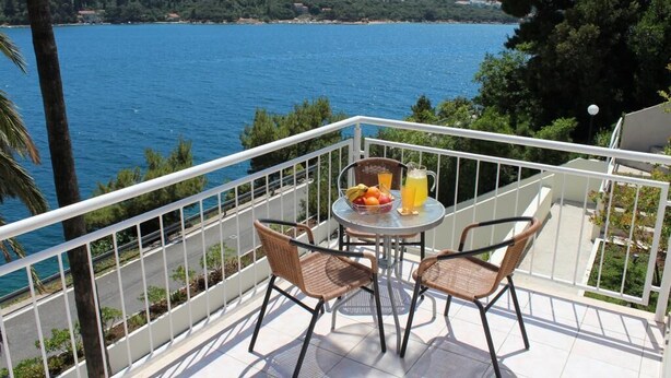 A balcony with wicker chairs and a table, overlooking a body of water and a distant coastline. - Apartments Lozica - Standard Studio Apartment with Terrace and Sea View (Mokosica)