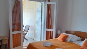 Een slaapkamer met een bed, een stoel, een tafel en een schuifdeur naar een buitenruimte.