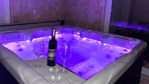 Een jacuzzi met een fles wijn en twee glazen, met een stenen muur op de achtergrond.