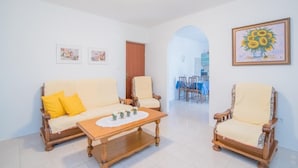 A living room with a sofa, two armchairs, a coffee table, and a painting of sunflowers.