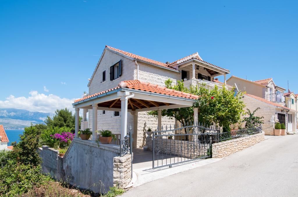 A two-story house with a stone facade, a tiled roof, and a covered porch with a metal railing.