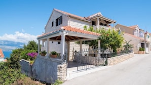 A two-story house with a stone facade, a tiled roof, and a covered porch with a metal railing.