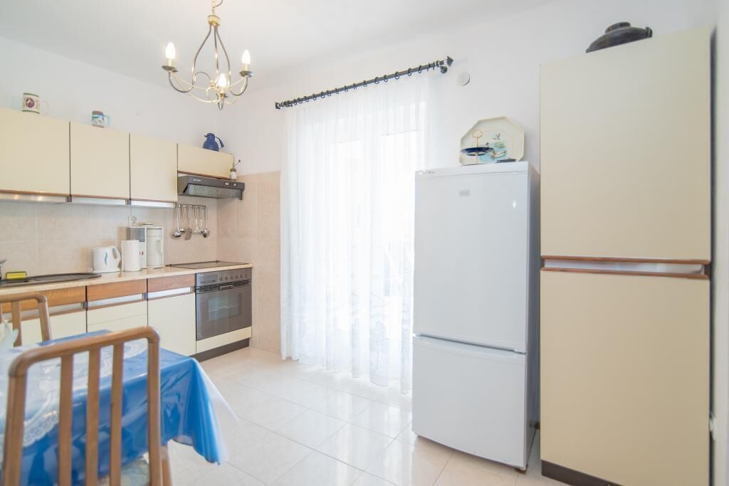 Una cucina con un tavolo da pranzo, sedie, un frigorifero e una finestra con tende.