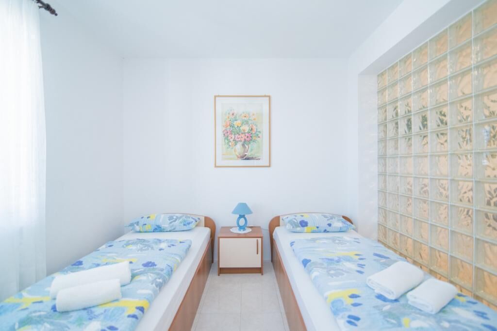 Camera d'albergo con due letti singoli, un comodino con una lampada, un quadro floreale appeso alla parete e una finestra vista giardino.