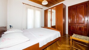 Een slaapkamer met een houten bed, een nachtkastje, een houten garderobe en een spiegel.