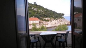 Un balcon avec une table et des chaises donnant sur une zone côtière, avec une colline rocheuse et un bâtiment doté d’un toit rouge.
