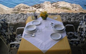 Una mesa lista para comer con vista al mar y a las rocas.