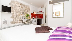 Ein Schlafzimmer mit einem großen Bett, einer Wand aus Stein, einer Küchenzeile und einem an der Wand befestigten Fernseher.