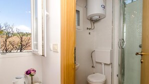 Ein Badezimmer mit Toilette, Dusche und einem Fenster mit Blick auf Bäume.