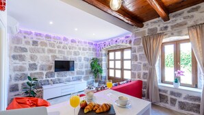 A breakfast setup with croissants, juice, and coffee on a white table in a stone-walled room with a TV and a window with curtains. - Apartments None & Nono-Comfort One-Bedroom Apartment with Shared Terrace (Cavtat)